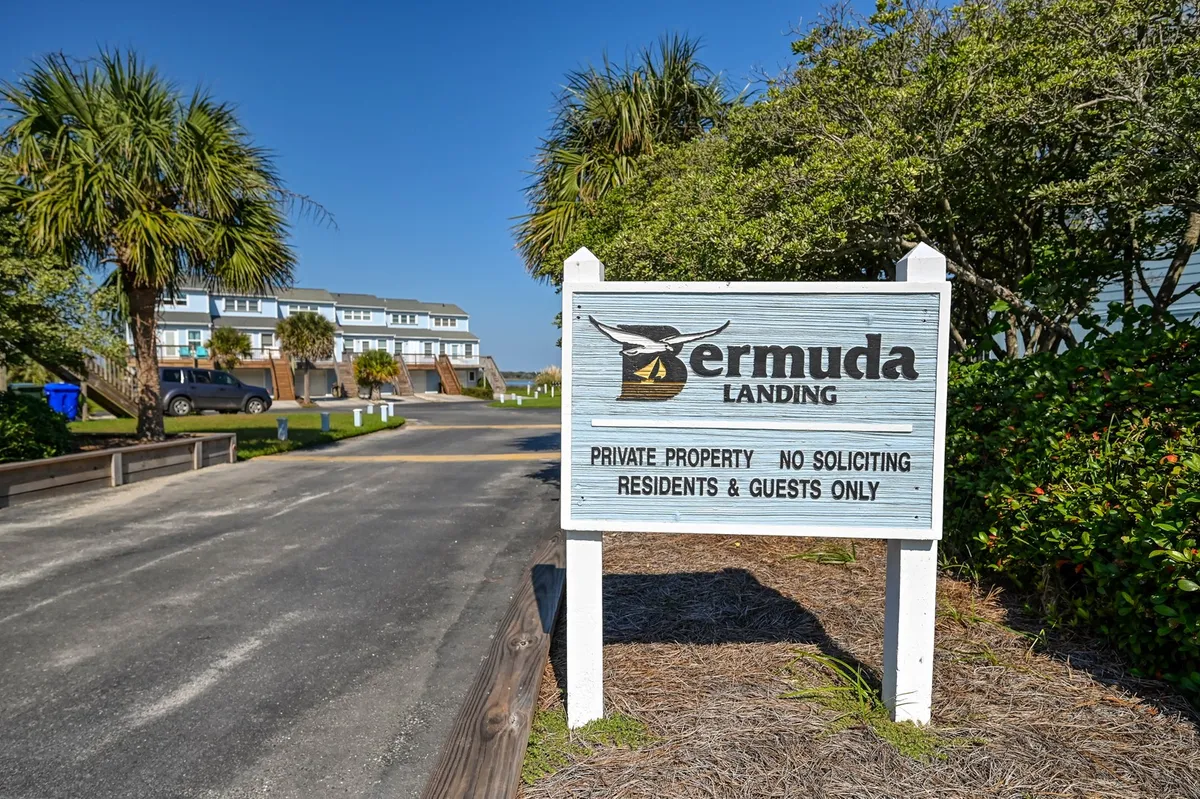 A welcoming sign for Bermuda Landing is surrounded by palm trees and a quiet road that winds into the property. The atmosphere is calm and inviting, with a hint of community spirit from the signage and landscape.