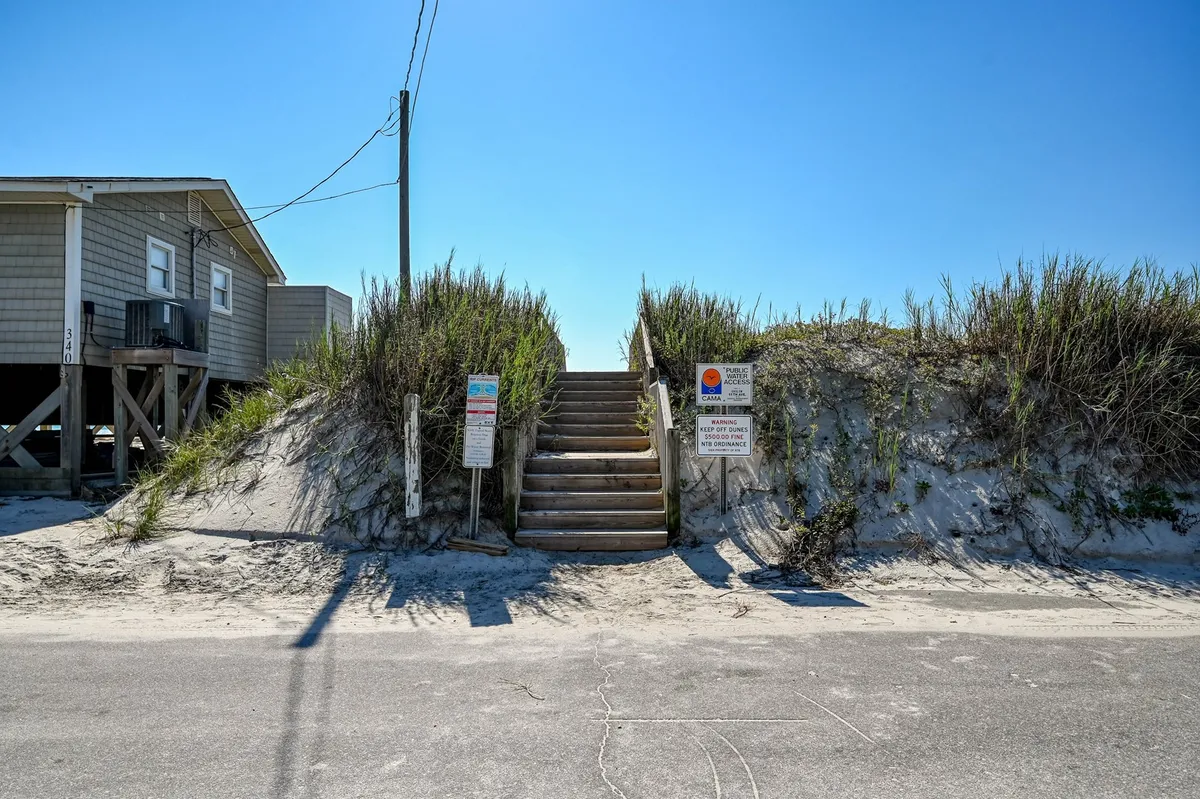 A wooden staircase leads through lush dune grass directly to the sandy beach, with clear signs indicating beach access. The scene is inviting, natural, and highlights the easy, family-friendly path from the home to the ocean.
