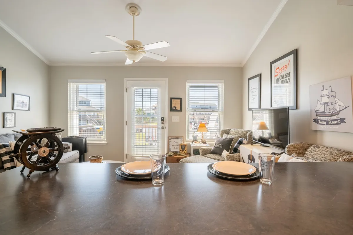 A cozy dining area with a set table, a sofa seating space nearby, large windows letting in natural light, and tasteful wall art. The layout encourages both shared meals and casual conversation, with easy sightlines between dining and lounging zones.