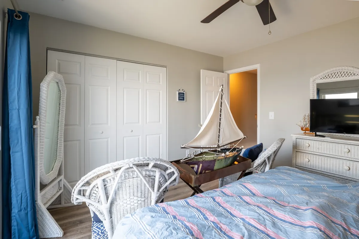 A serene bedroom with a bed covered in a striped blanket, decorative sailboat accents, woven chairs, and a TV unit. The decor is inviting and restful, with light streaming in to create a cozy atmosphere perfect for unwinding after a day of adventure.