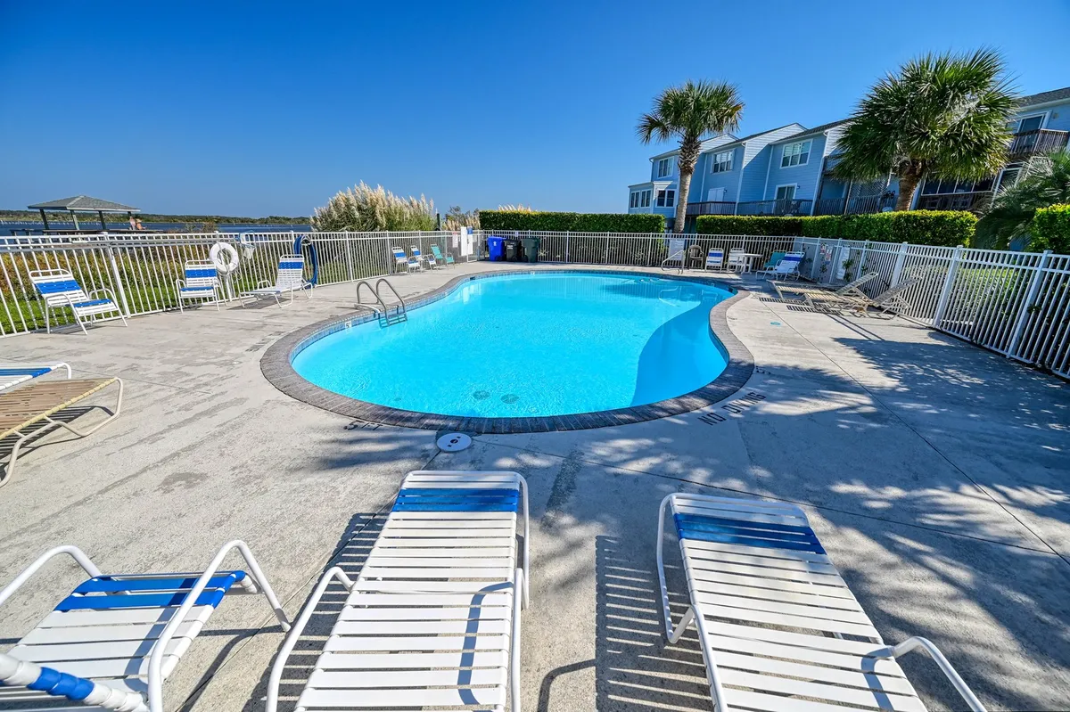 A sparkling community swimming pool is surrounded by lush greenery and lined with an array of comfortable lounge chairs. The inviting space offers ample room for residents to swim, sunbathe, or relax with friends. The atmosphere is leisurely, with hints of sunset lighting warming the scene.